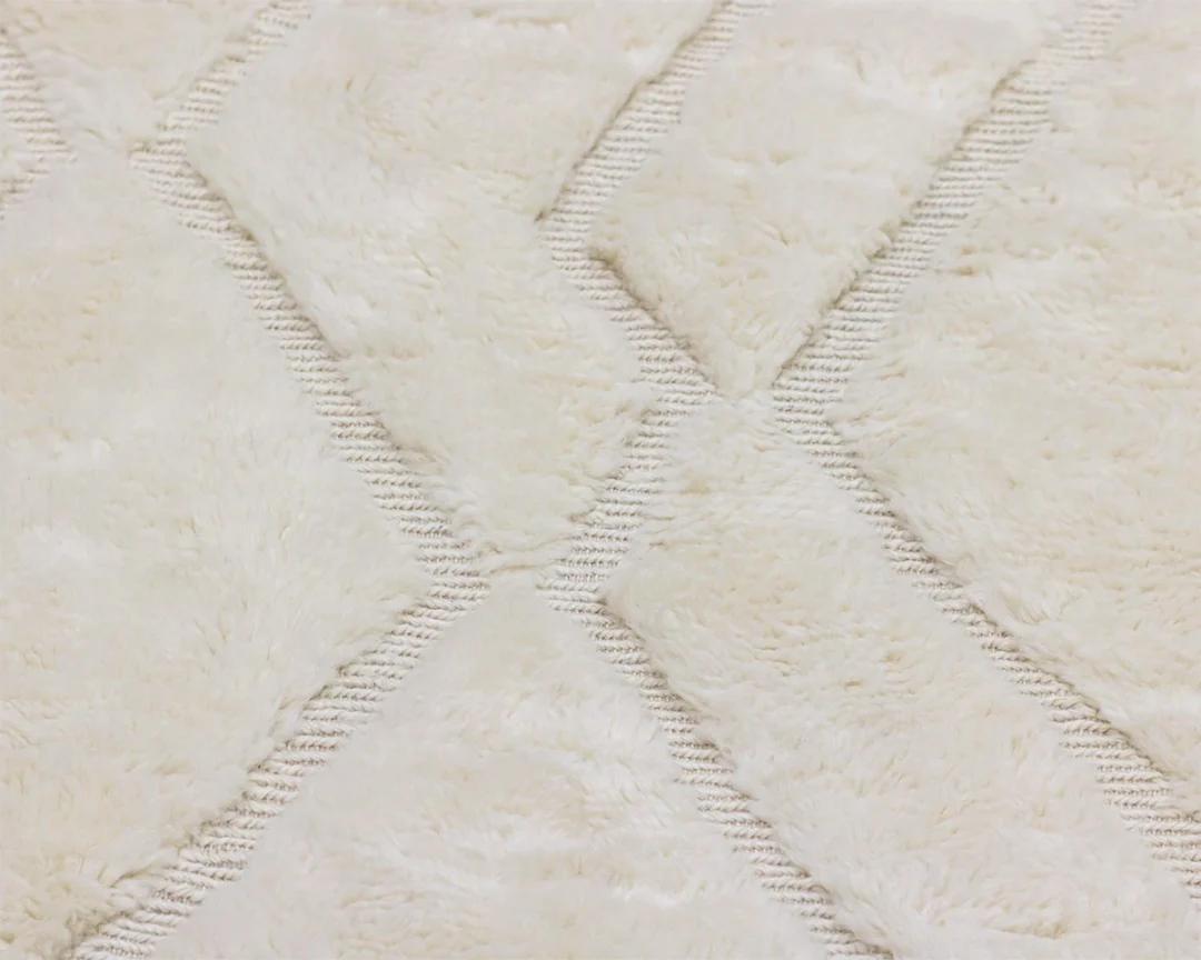 Close-up of a cream-colored, textured rug with a geometric diamond pattern and slightly raised, fluffy sections.