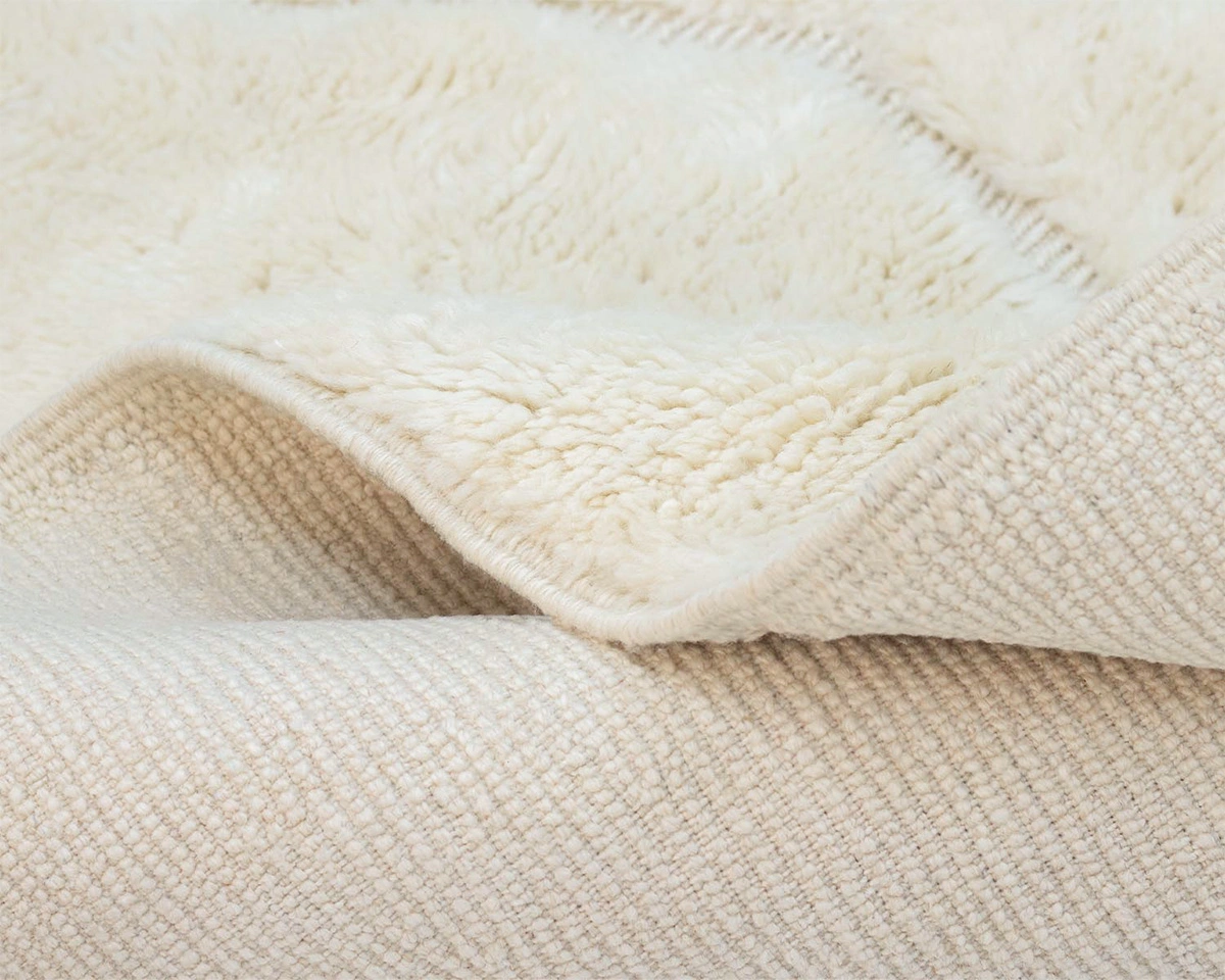 Close-up of a beige textured rug with a soft, fluffy surface showing both the woven underside and the plush upper side.