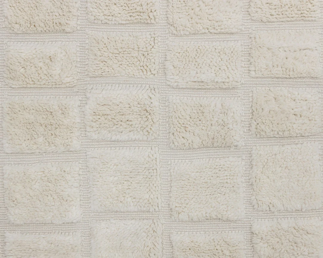 Close-up of a textured, cream-colored rug with a grid pattern of raised, fluffy square sections.