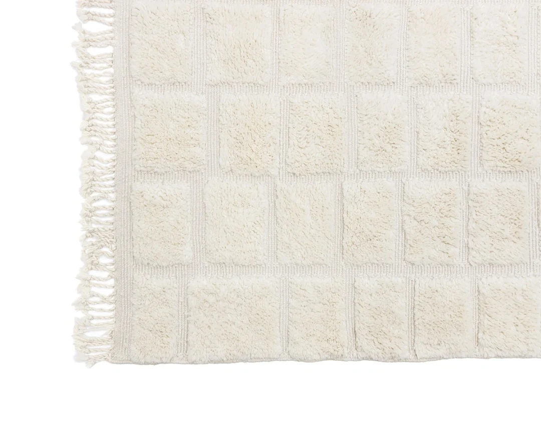 Off-white textured rug with a grid pattern and fringed edging on the left side.