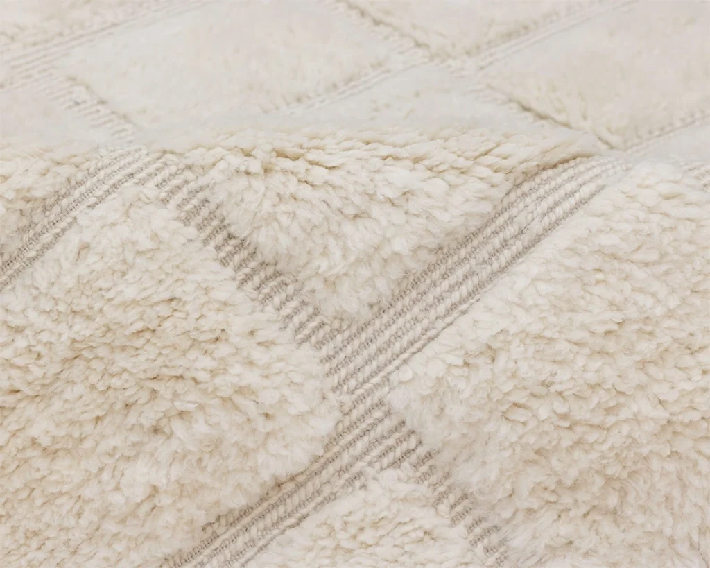 A close-up view of a cream-colored, textured, and fluffy fabric rug with a subtle checkered pattern.