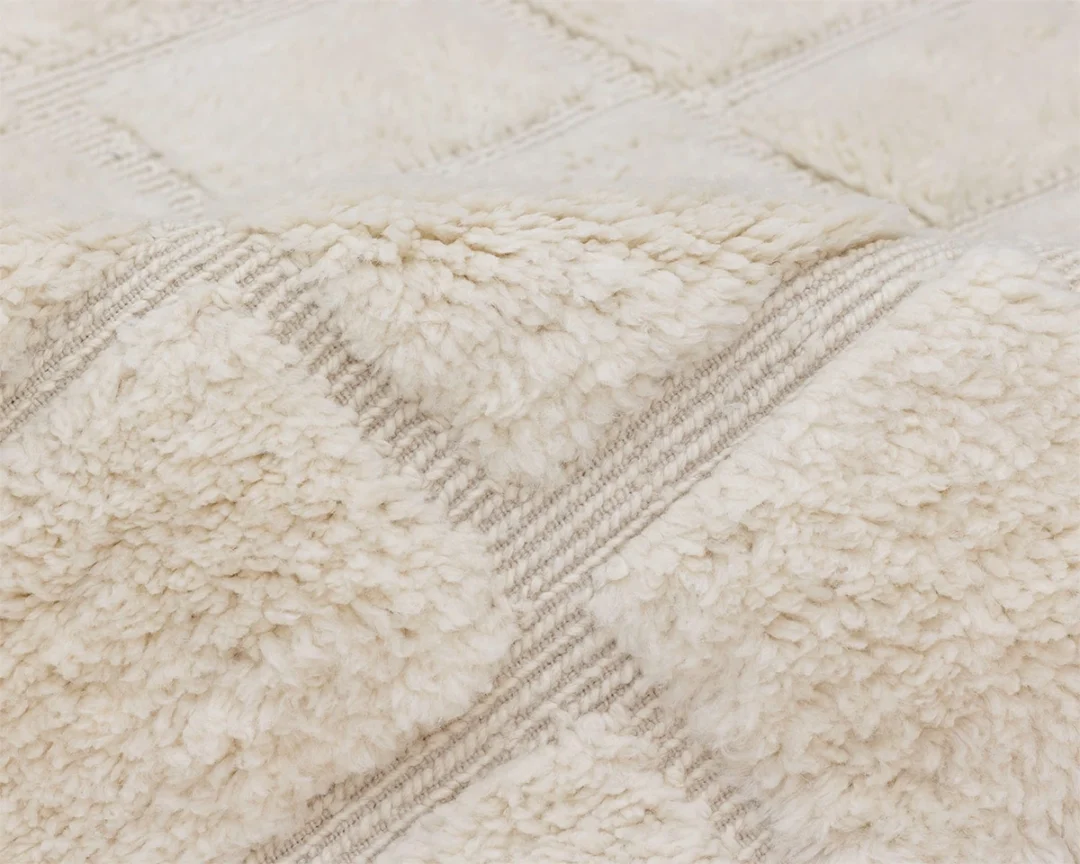 A close-up view of a cream-colored, textured, and fluffy fabric rug with a subtle checkered pattern.