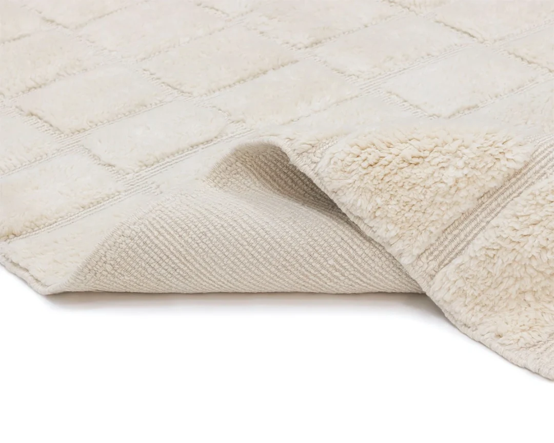 A close-up of a cream-colored, textured rug with one corner lifted to show the underside and surface details.