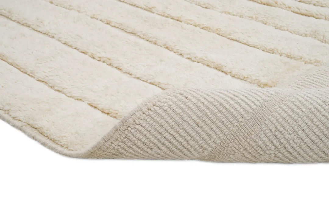 Close-up of a cream-colored textured rug, partially folded to show the soft, plush top surface and the woven underside.