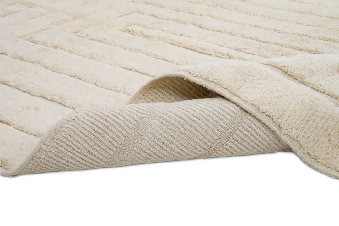 Cream-colored textured area rug with one corner flipped over, showing the woven underside and soft, plush surface on top.