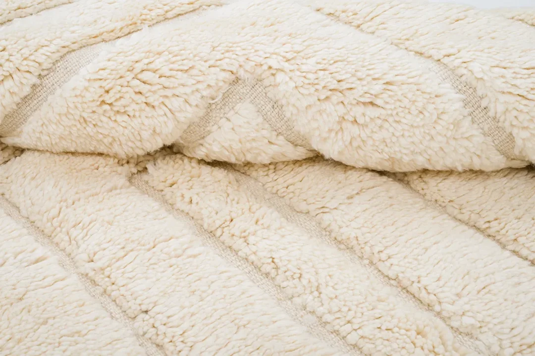 A close-up view of a cream-colored, textured, fluffy blanket with horizontal stitching details.