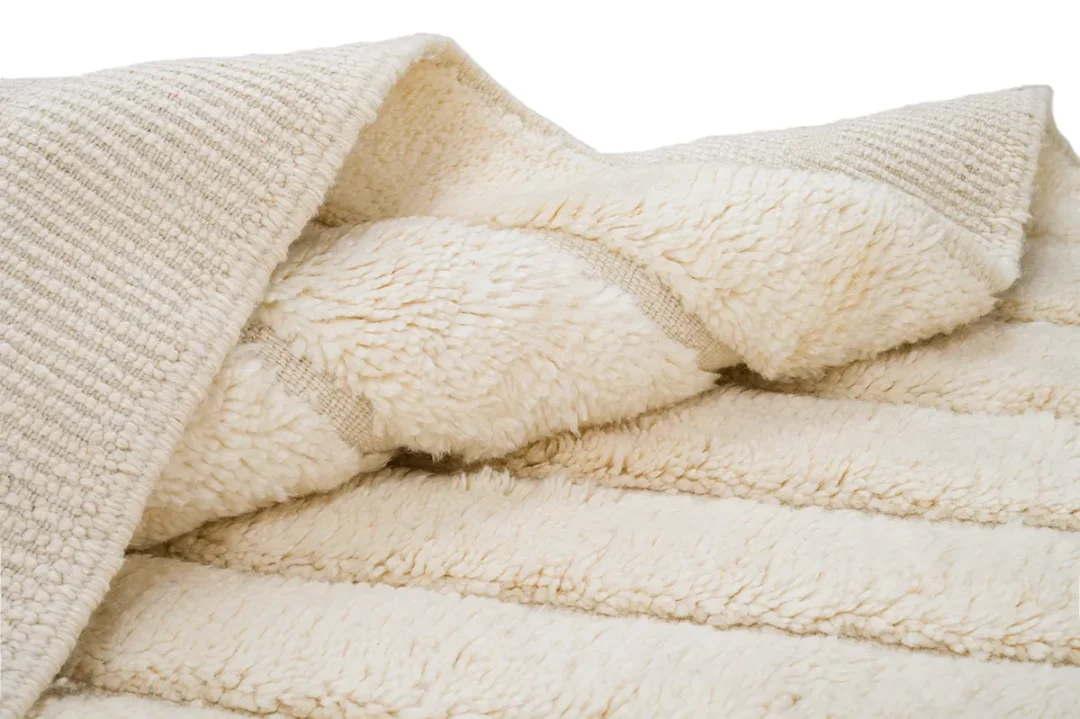 A close-up of a folded, cream-colored, textured, and fluffy blanket with soft, thick pile and ribbed pattern on a white background.