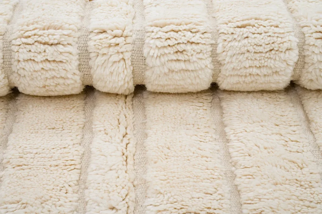 A close-up view of a cream-colored, plush, textured rug with thick, soft ridges and a fluffy appearance.