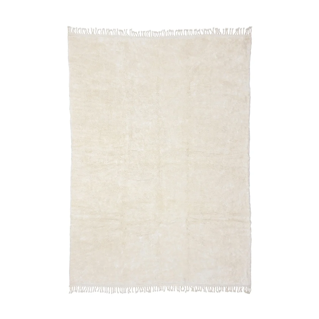 A rectangular, off-white area rug with a soft texture and fringes on the shorter edges, viewed from above against a white background.
