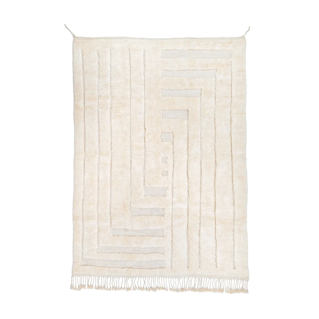 A rectangular cream-colored rug with geometric line patterns and short fringe along the bottom edge, hanging against a white background.