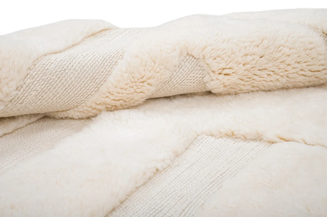 Close-up of a cream-colored, plush, textured rug with ribbed and fluffy sections.