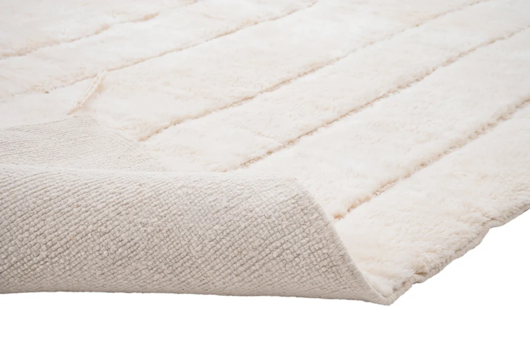 A close-up view of a cream-colored, plush, textured rug with one corner lifted to show the woven underside.