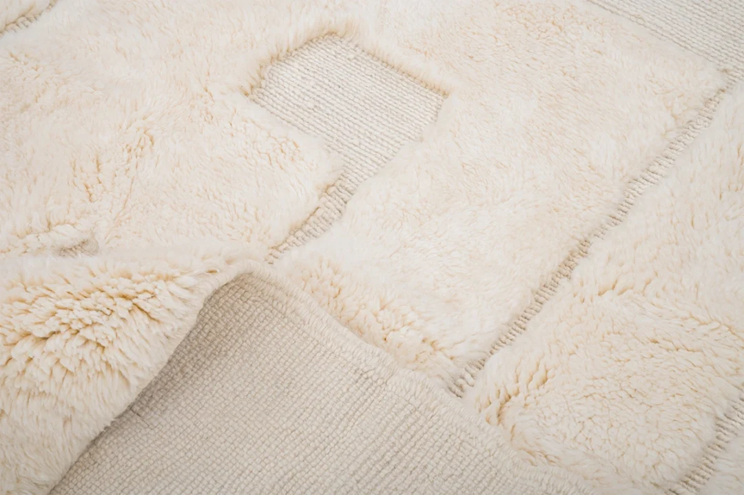 Close-up of a textured cream-colored rug with square patches of fluffy and flat woven sections, including a square cutout in the center.