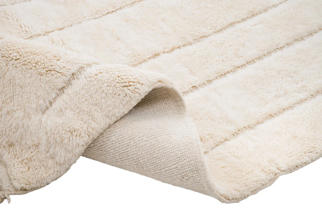 A close-up of a cream-colored, textured area rug with one corner slightly folded over, showing the backing.