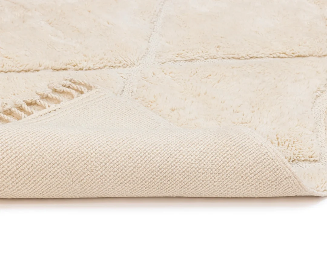 Close-up of a cream-colored textured rug with a soft, plush surface and a woven underside, partially flipped to show both sides.
