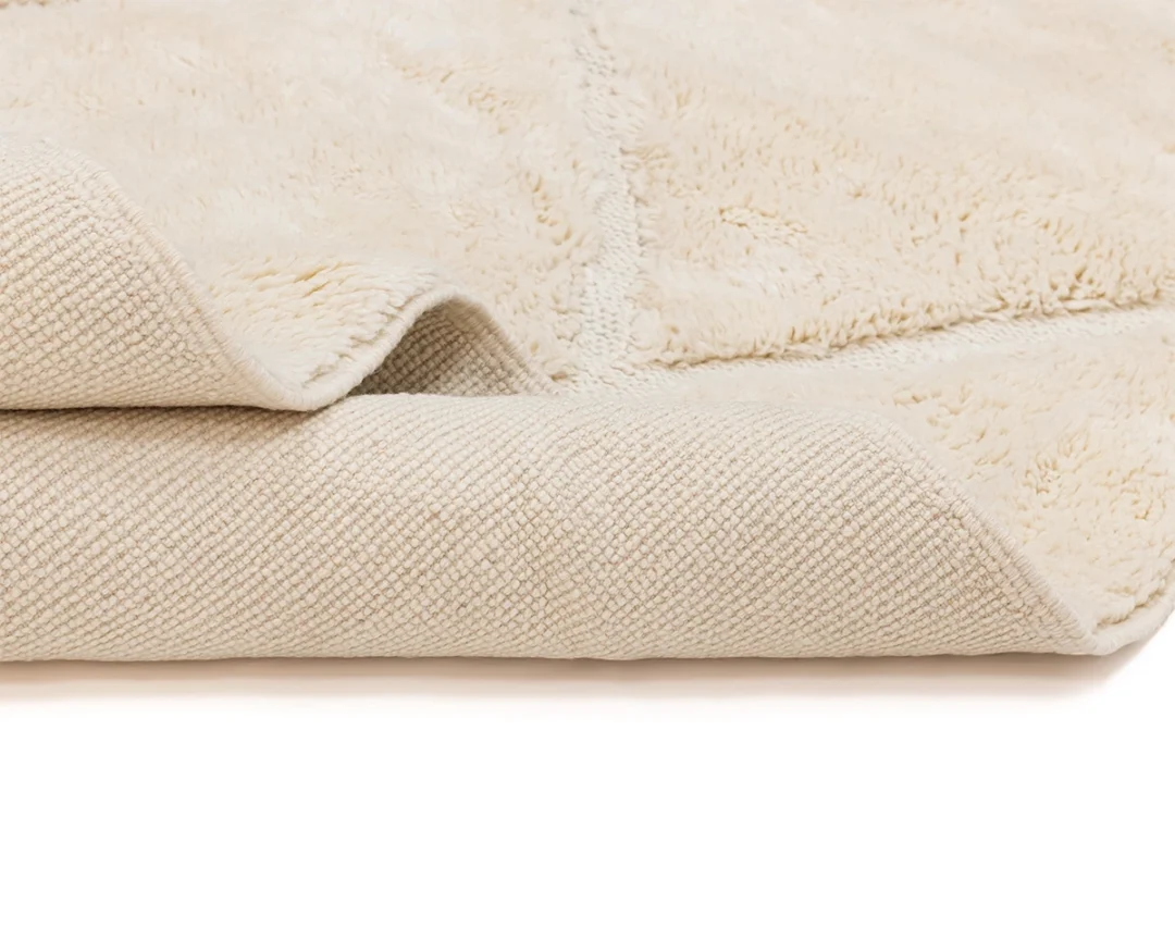 A close-up view of a beige, textured blanket or rug, showing both the soft, plush side and the woven backing.