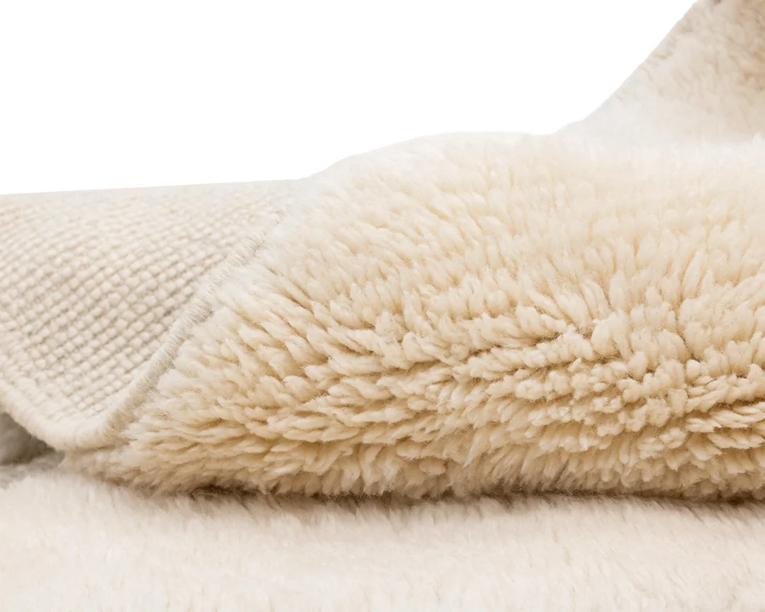 Close-up of a folded, cream-colored, fluffy sherpa or fleece blanket showing its soft, textured surface.