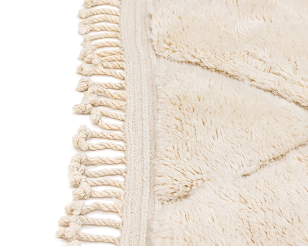 Close-up of a cream-colored, textured rug with a geometric pattern and twisted fringe along one edge.