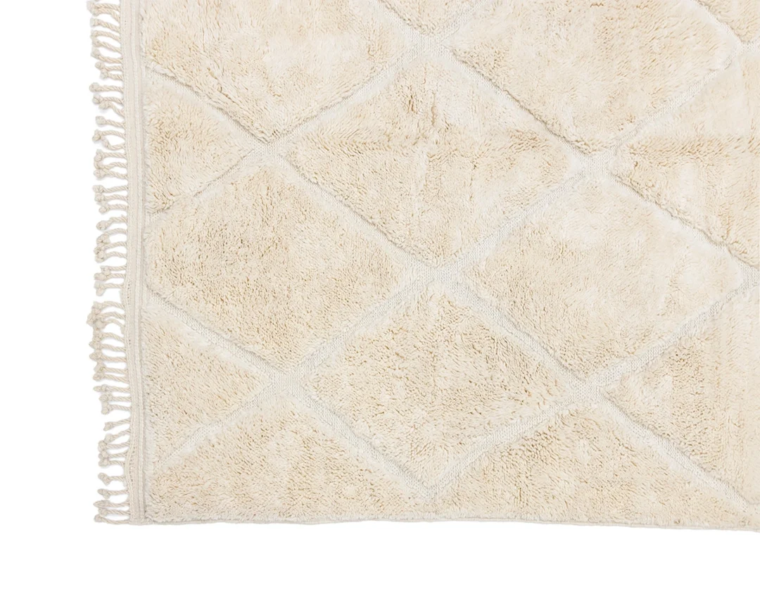 Close-up of a beige textured rug with a diamond pattern and fringe along the left edge.