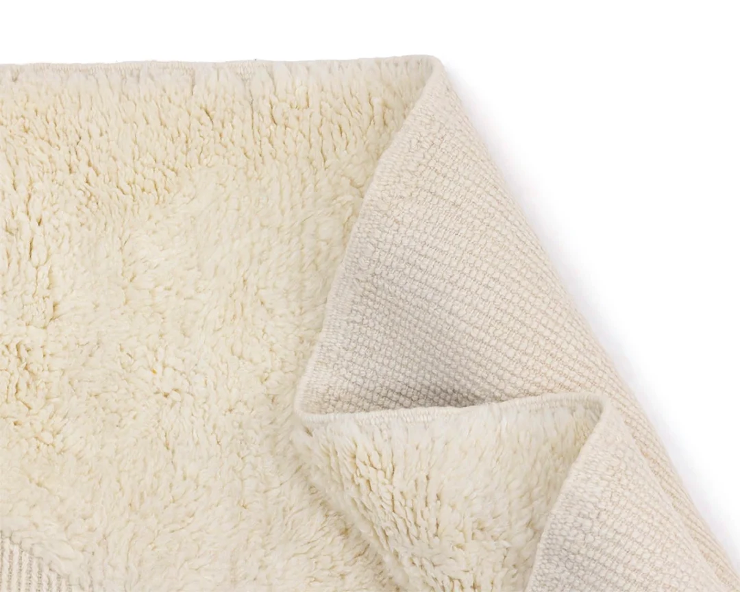 A close-up of a cream-colored, textured rug with one corner folded over to show both the plush front and woven back sides.