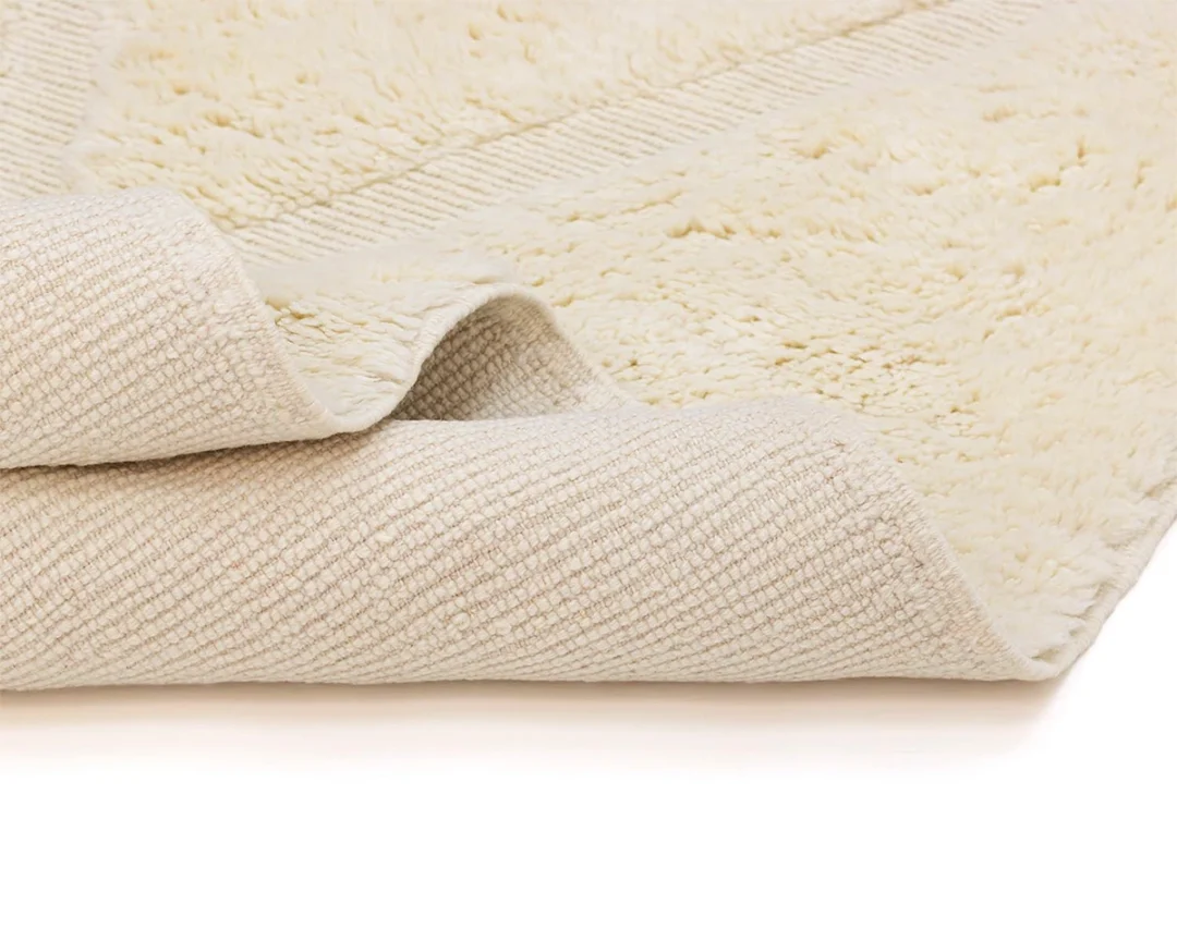 Close-up of a folded, off-white textured rug showing both its plush and woven sides against a plain background.