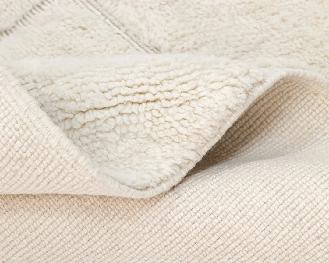 Close-up of a folded cream-colored textured blanket showing its soft, fluffy inner lining and woven outer surface.
