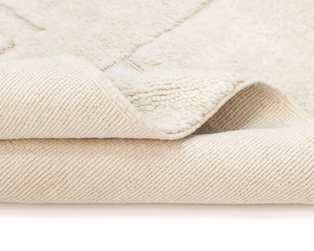 Close-up of a cream-colored rug with one corner folded over, showing the textured backside and soft, plush surface on top.