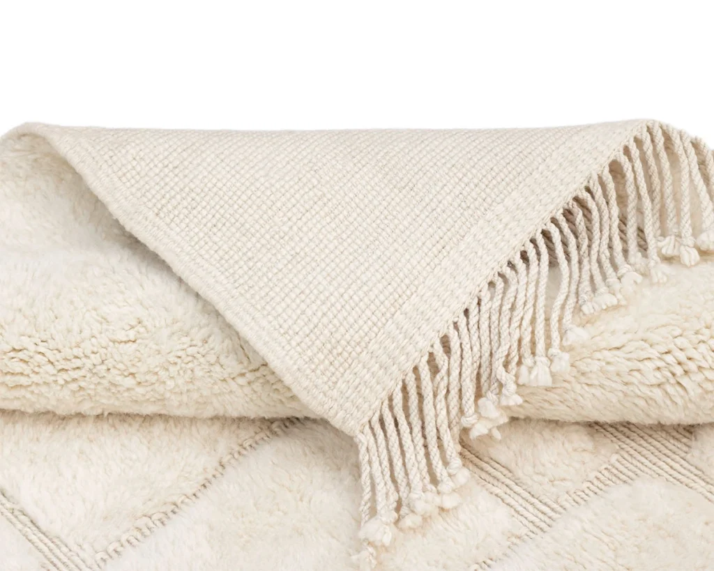 A folded cream-colored textured blanket with diamond patterns and fringe along one edge.