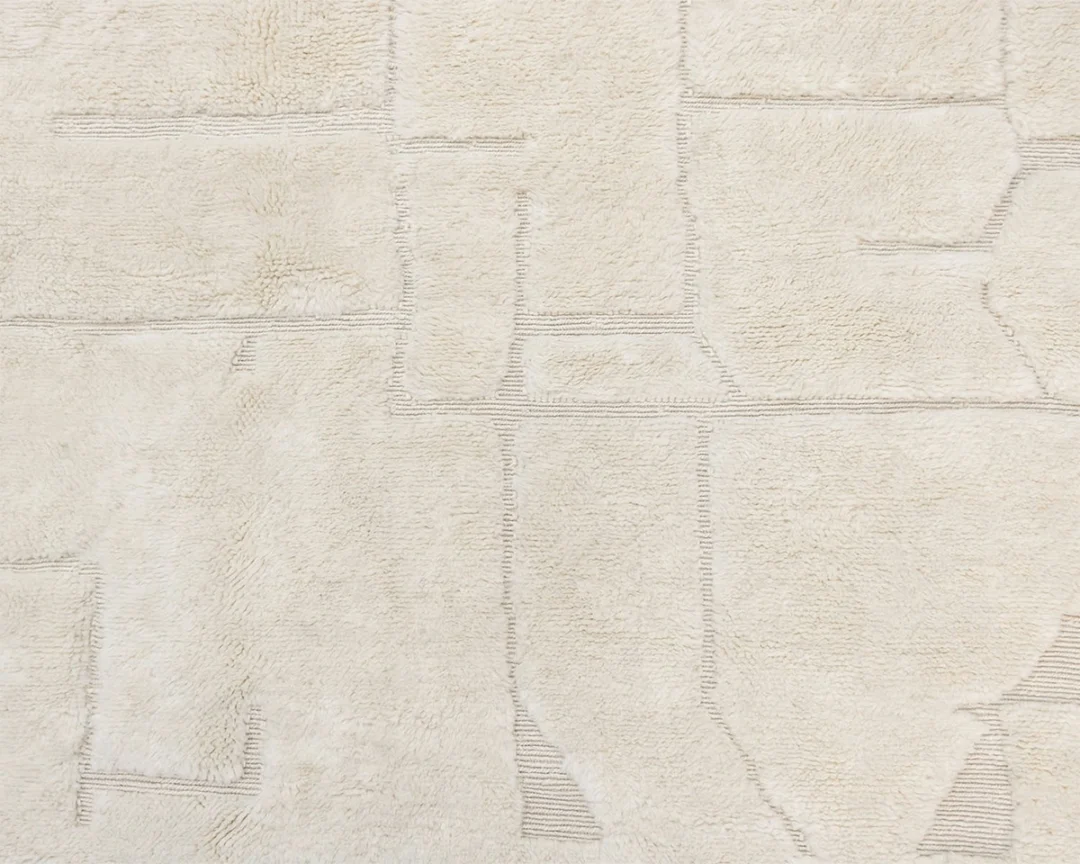 Close-up of a cream-colored textured rug with subtle abstract geometric patterns and stitched lines.