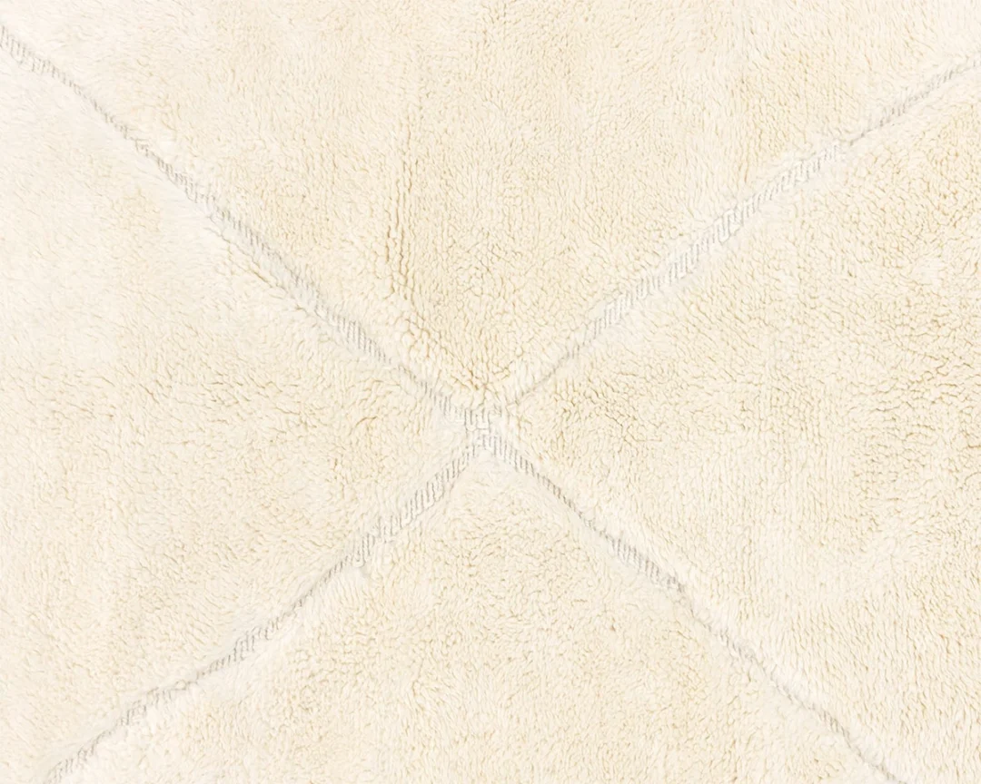 Close-up view of a textured cream-colored rug with intersecting decorative lines forming an X pattern.