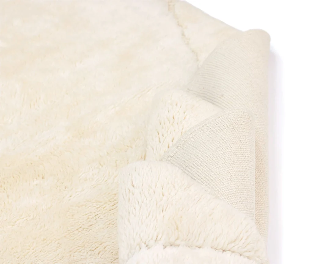 A close-up of a cream-colored, fluffy rug with one corner partially folded over, revealing the textured backing.