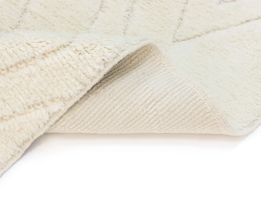 A close-up of the corner of a cream-colored rug folded over, showing its textured surface and woven underside.