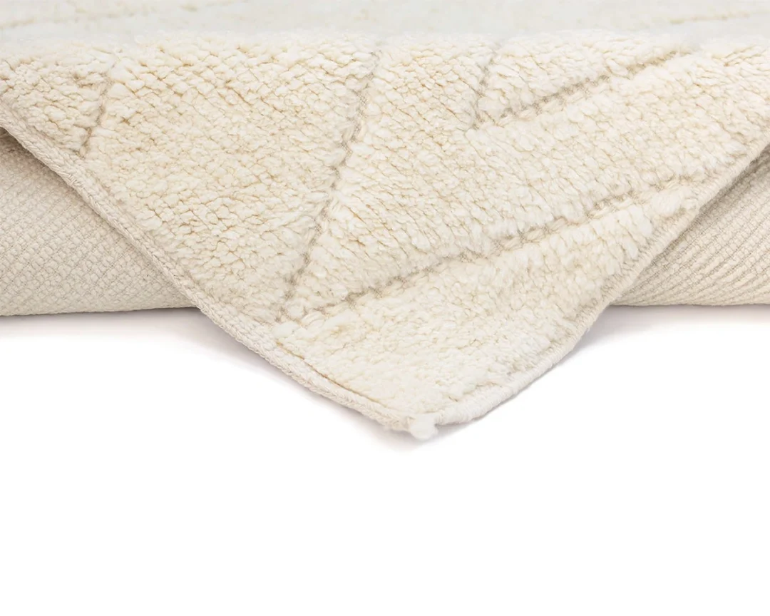 Close-up of a cream-colored, textured rug with a geometric pattern, showing the edge folded over to reveal the backing.