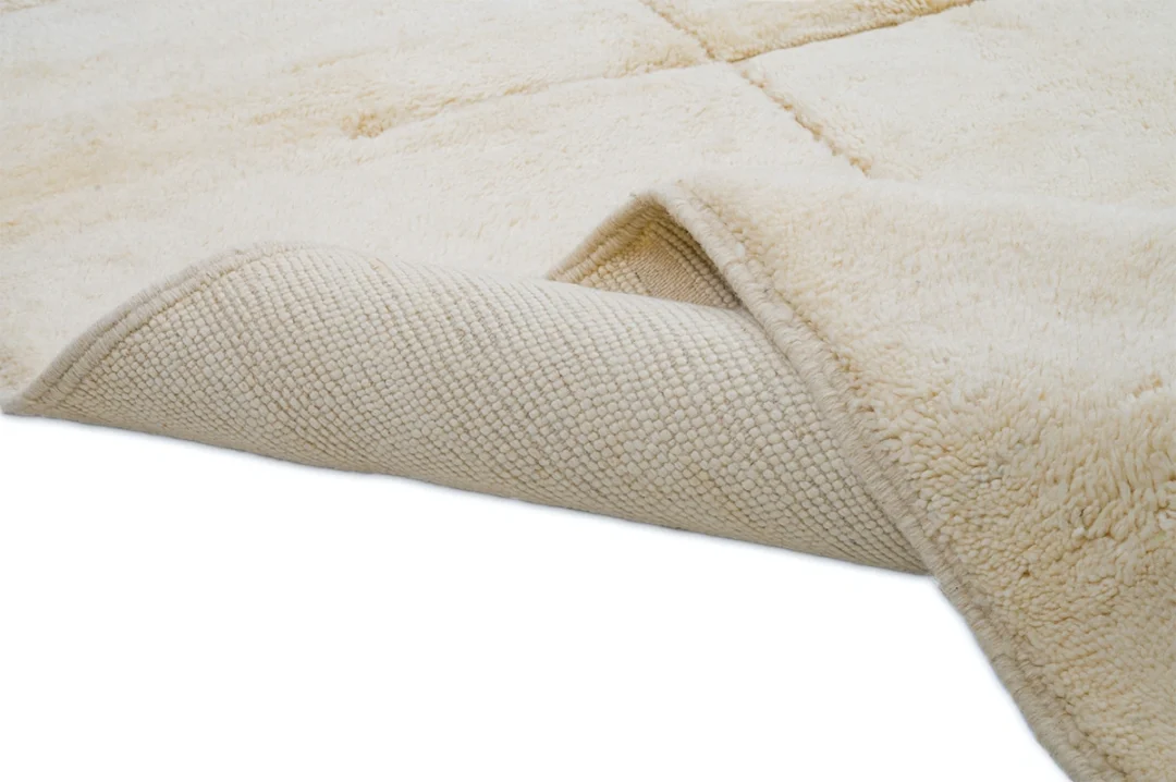 A close-up of a cream-colored rug with one corner folded back, showing the textured underside and plush surface.