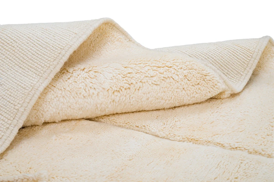 A close-up view of a cream-colored, textured blanket with a soft, plush lining and a woven outer layer.