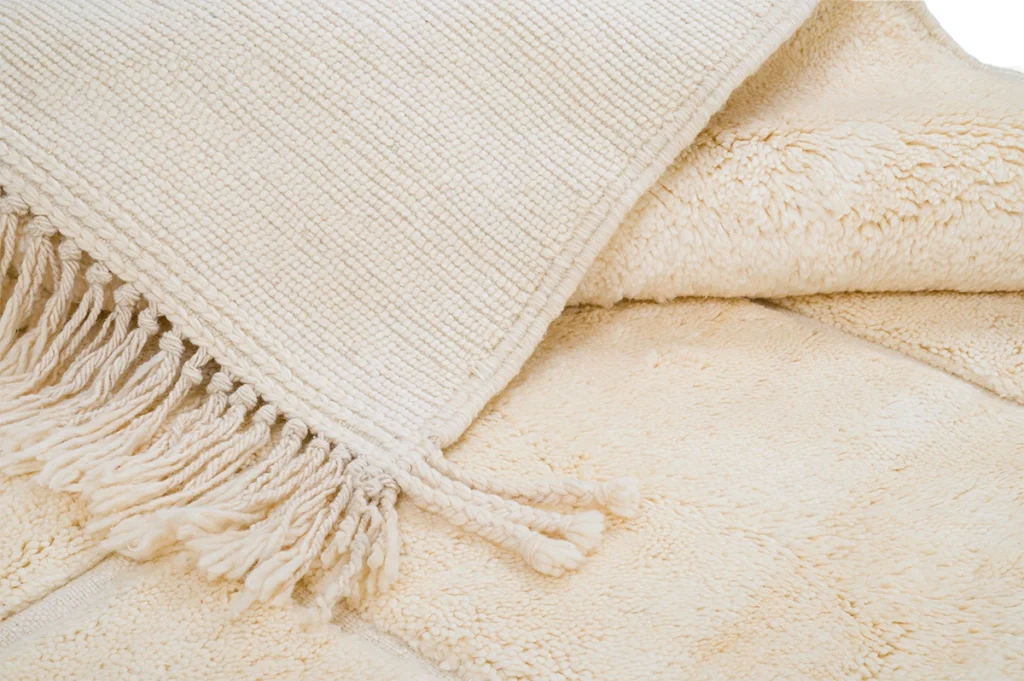 Close-up of a cream-colored woven blanket with fringe detail, layered over a soft, plush beige blanket.