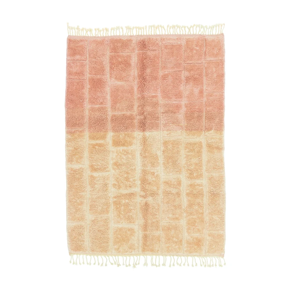 A rectangular rug with a grid pattern, gradient colors from pink at the top to beige at the bottom, and white fringe on both short edges.