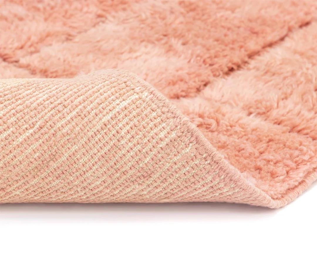 Close-up of a pink, fluffy rug with one corner lifted to show the textured underside.