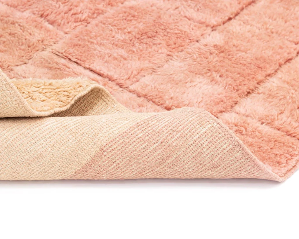 A close-up of a pink, plush, textured rug with one corner partially folded to reveal the backing.