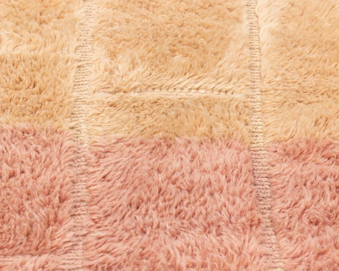 Close-up of a textured fabric with alternating tan and pinkish-beige rectangular sections and visible stitching between the sections.