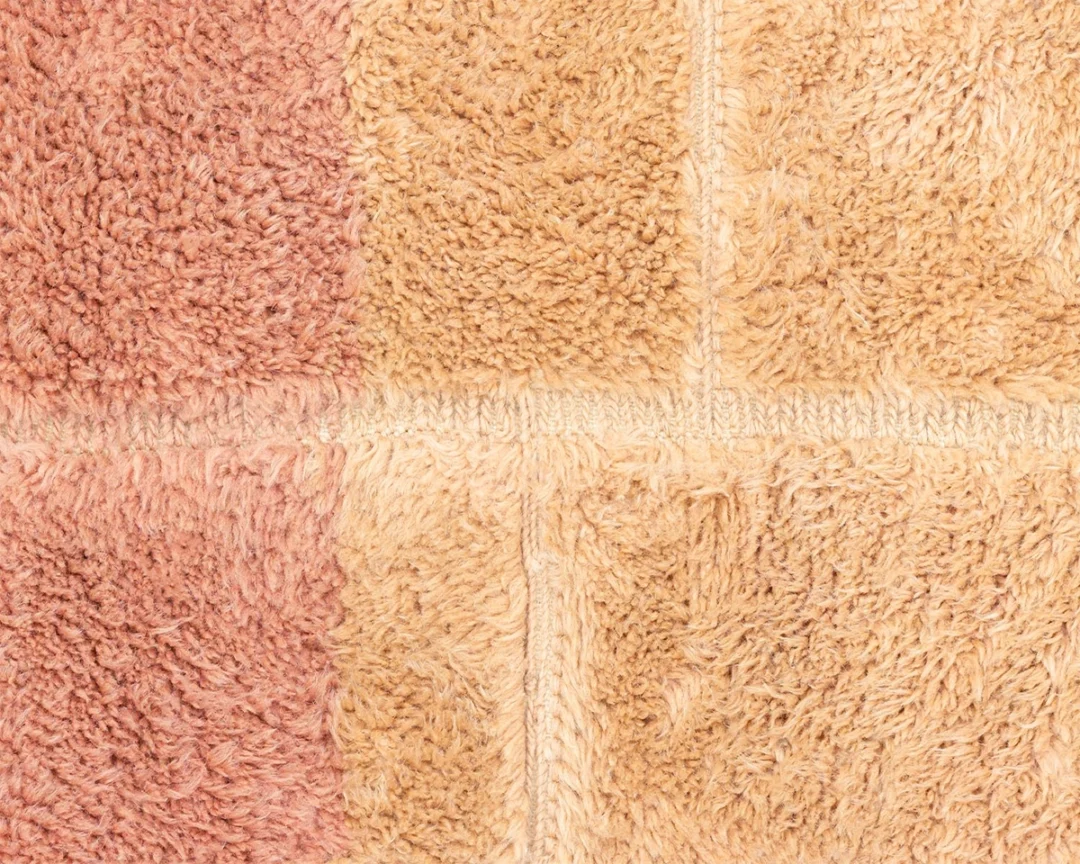 Close-up of a soft, textured fabric with a checkered pattern in shades of beige and brown. The material appears to be terry cloth or a similar textile.