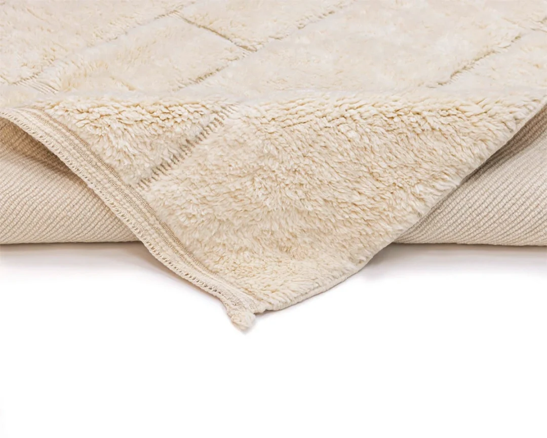 A close-up view of a beige, fluffy, fleece blanket partially folded back to show its soft texture and stitched edging.