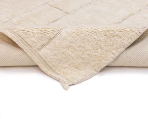 A close-up view of a beige, fluffy, fleece blanket partially folded back to show its soft texture and stitched edging.