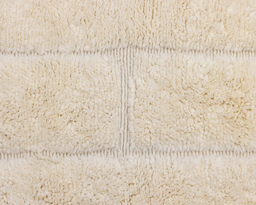 Close-up view of a beige, textured, fluffy fabric with horizontal and vertical stitch lines creating a subtle grid pattern.