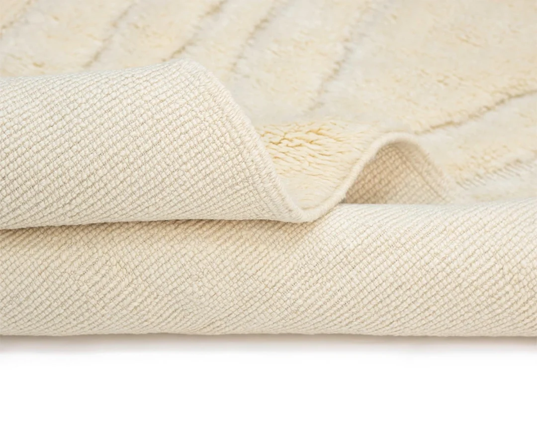 A close-up of a folded, cream-colored textured rug showing both the front and back sides.