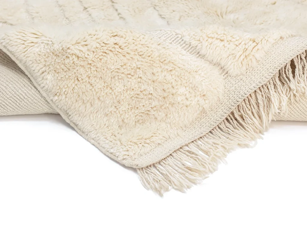A close-up of a cream-colored, fringed throw rug showing its soft, textured surface and woven underside.