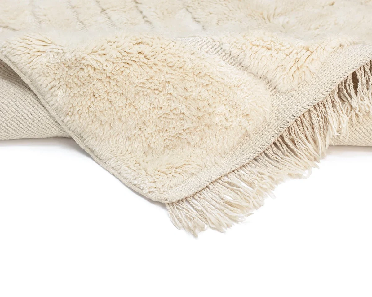 A close-up of a cream-colored, fringed throw rug showing its soft, textured surface and woven underside.