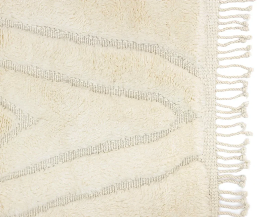 Close-up of a cream-colored textured rug with wavy line patterns and fringed edges on one side.