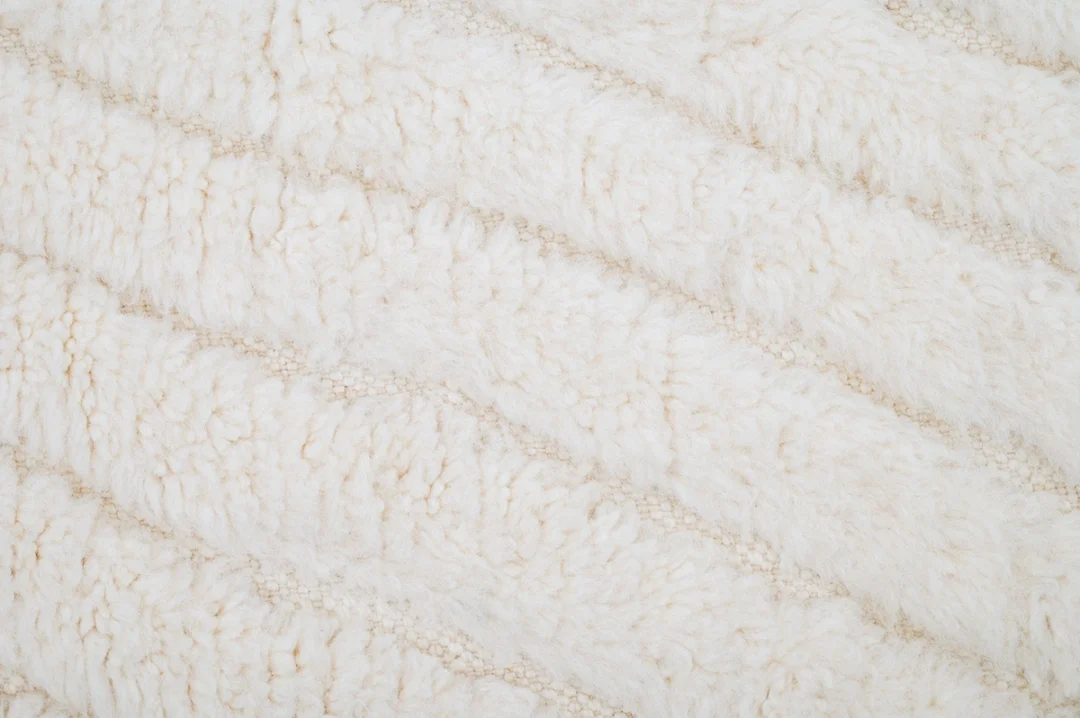 Close-up of a cream-colored, textured fabric with a soft, fluffy surface and diagonal seam lines.