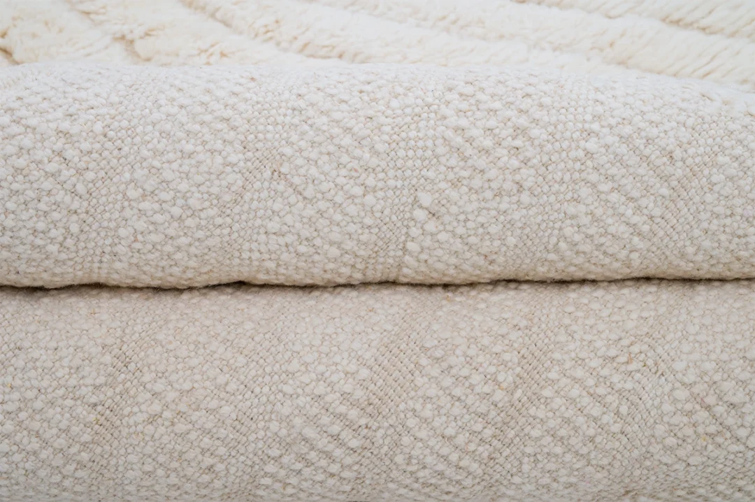 Close-up view of two beige, textured, woven blankets stacked on top of each other, showing their detailed patterns and fibers.
